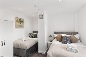 a bedroom with two beds and a clock on the wall at Sleek & Stylish Apartment in the Best Area in Beckenham