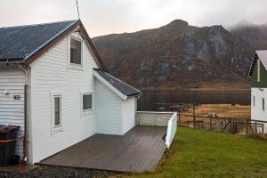 a white house with a wooden deck in front of a mountain at Heimly, cosy house in a fjord in Bjørnsand