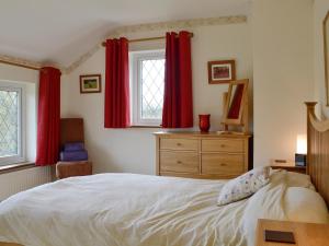 Schlafzimmer mit roten Vorhängen, einem Bett und einer Kommode in der Unterkunft Oak Tree Cottage - E5062 in Lydbrook