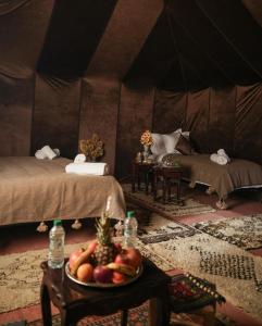 a room with two beds and a bowl of fruit on a table at Merzouga Glossy Camp in Merzouga