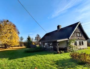 an old house with a black roof on a green field at Na Żurawim Wzgórzu in Pasym