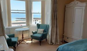 a bedroom with a bed and chairs and a view of the ocean at Kings' House in Douglas