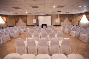 una sala de conferencias con sillas blancas y una pantalla en Hotel El Camino Inn & Suites en Reynosa