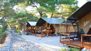 un grupo de lodges con mesas y sillas frente a los árboles en Losinj Glamping - Camp Čikat - Wild, en Mali Lošinj