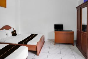 a bedroom with two beds and a desk with a television at Collection O near Universitas Negeri Padang formerly Hotel Amra in Padang