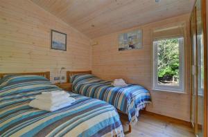two beds in a room with wooden walls and a window at Milliners Lodge in Kelling
