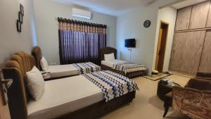 a bedroom with two beds and a couch and a tv at Airport Gateway Guesthouse in Rawalpindi