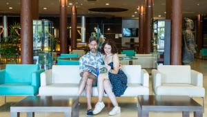Un hombre y una mujer sentados en sillas en un vestíbulo en Evenia Olympic Palace, en Lloret de Mar