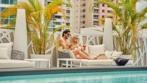 een man en een vrouw die in stoelen naast een zwembad zitten bij Gran Evenia Panamá Hotel in Panama-Stad