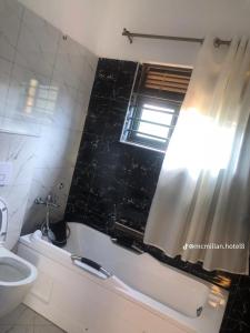 a bathroom with a tub and a toilet and a window at McMillan Hotel in Entebbe +6 photos