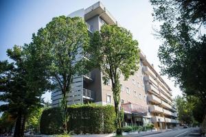 a tall building with trees in front of a street at Hotiday Conegliano in Conegliano