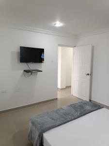 a white bedroom with a bed and a flat screen tv at Apto San José in Armenia