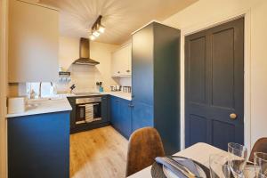 een keuken met blauwe kasten en een tafel met stoelen bij Host & Stay - Daisy Cottage in Masham
