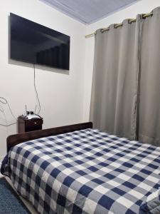 a bedroom with a bed with a checkered blanket and a tv at House - Cantinho de Jacaré in Jacarèzinho
