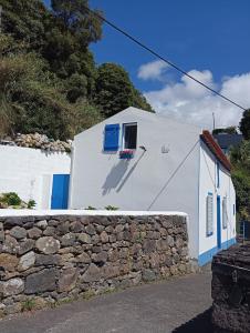 ein weißes Gebäude mit blauen Fenstern und einer Steinmauer in der Unterkunft Ribeira da Praia House in Vila Franca do Campo