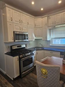 a kitchen with white cabinets and a stove and a table at Cozy Getaway in Kearny