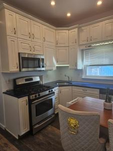 a kitchen with white cabinets and a stove and a table at Cozy Getaway in Kearny