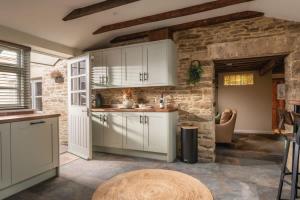 a kitchen with white cabinets and a stone wall at Homestead - Cosy Cotswolds Cottage with Hot Tub in South Cerney
