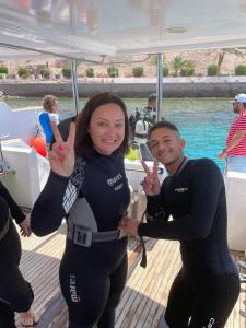 a man and woman giving the peace signs on a boat at Camel Dive Club By The Sea Inn in Jurf ad Darāwīsh