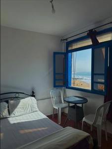a bedroom with a bed and a table and a window at Laverie du Soleil Surf House in Taghazout