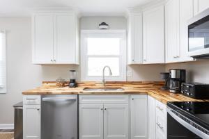 une cuisine avec des armoires blanches, un évier et une fenêtre dans l'établissement Newly Updated Cottage in the Heart of KDH, à Kill Devil Hills 26 autres photos