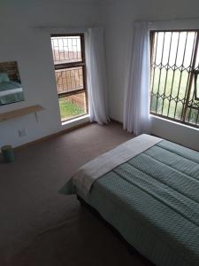 a bedroom with a bed and two large windows at BushWave in Jeffreys Bay