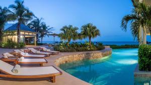 a resort swimming pool with lounge chairs and the ocean at Villa Oasis Anguilla in Long Bay Village