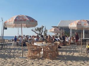 eine Gruppe von Personen, die an Tischen unter Sonnenschirmen am Strand sitzen in der Unterkunft Cosy beach cottage in Zandvoort