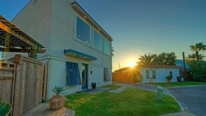 a house with the sun setting behind a fence at Modern Coastal Home w Balcony Views Firepit Prime Port A Location Casa Blanca by AvantStay in Port Aransas