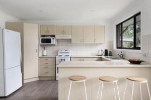 a kitchen with white appliances and two stools at Lakeside Getaway Halekulani in Budgewoi