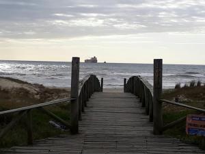 a wooden boardwalk leading to the ocean with a ship at summer house 2026 in Tramandaí +12 photos