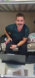 Un hombre sentado en una cama mirando una computadora en Gulf Gateway Hostel, en Mascate