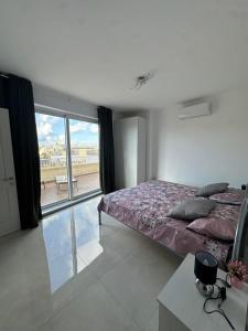 a bedroom with a bed and a large window at PrimeRose Penthouse in Sannat