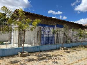 a fence with a tree in front of a building at Pousada Praça da Bíblia - Santa Maria da Vitória in Santa Maria da Vitória