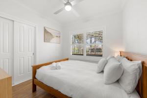 a white bedroom with a bed with white pillows at Dolphin Cove - Pet Friendly with Fireplace in Callala Bay