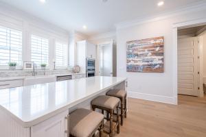a white kitchen with a large white counter and stools at Happily Eva After at Prominence 30A in Inlet Beach