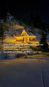 a house lit up at night in the snow at Таежный домик Васильево in Poperechnoye