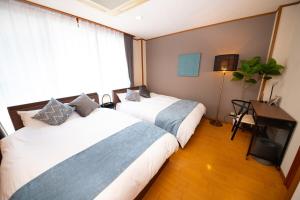ein Schlafzimmer mit zwei Betten und einem Schreibtisch und einem Fenster in der Unterkunft simasima-stay高松駅 ー 高松駅徒歩2分 無料駐車場ー in Takamatsu