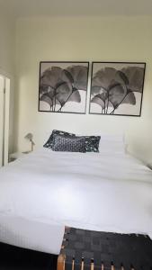 a bedroom with a white bed with three pictures on the wall at Healesville Gardener's Cottage in Healesville