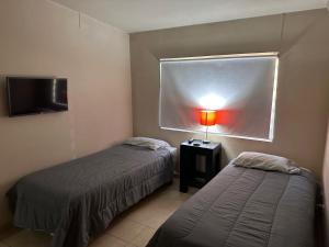 a bedroom with two beds and a window and a lamp at San Basilio Suites in Mexicali