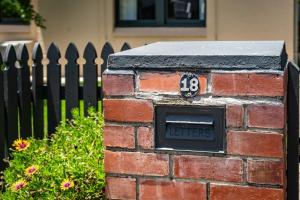 维克多港K Rose Cottage In the heart of Victor Harbor - No Linen Included的一道砖墙，墙上挂着一块牌子，牌子前面是一道栅栏。