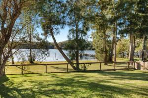 a fence next to a body of water with trees at Lakeside - relaxed 3 BR waterfront retreat in Burrill Lake