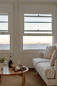 a living room with a couch andwindows with sailboats in the ocean at Fogo @ Ethel & Ode’s in Bundeena +15 photos