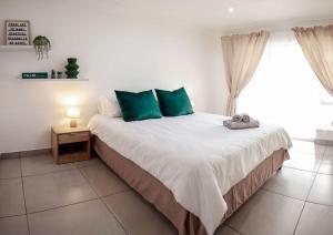 a bedroom with a bed with green pillows and a window at Neptunes Hideaway in Jeffreys Bay