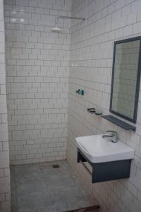 a white tiled bathroom with a sink and a mirror at Off Airport Kilimanjaro lodge in Boma la Ngombe