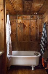La salle de bains est pourvue d'une baignoire et d'un plafond en bois. dans l'établissement Rustic Cabin Retreat on the Ten Mile River in Narrowsburg, New York, à Lava