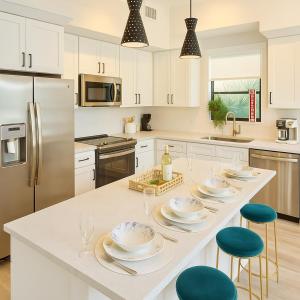a kitchen with white cabinets and a white island with plates and chairs at Lux place and cozy 3Beds 2Rooms enjoy life in WPB Gym, EV Station Nearby the downtown and beaches in West Palm Beach