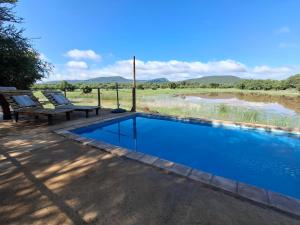 a swimming pool with two benches next to a river at Ou Kraal Tented Lodge in Boshoek