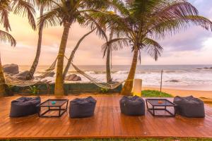 Una terraza de madera con sillas y palmeras y el océano. en Mask & Tide, en Ambalangoda