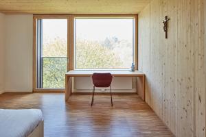 Ein Schlafzimmer mit einem Schreibtisch und einem roten Stuhl vor einem Fenster in der Unterkunft Tagungshotel Kloster Untermarchtal 